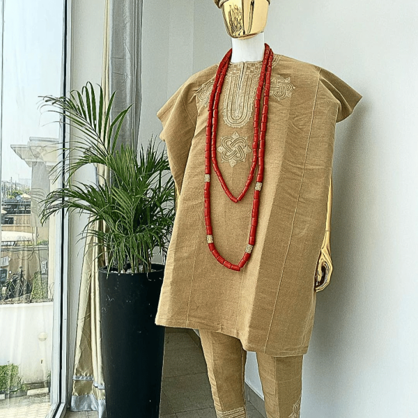 A champagne gold aso oke dashiki, with a floral and ancient style shaped embroidery design, hand woven Yoruba hat, an extra length red and gold coral bead.