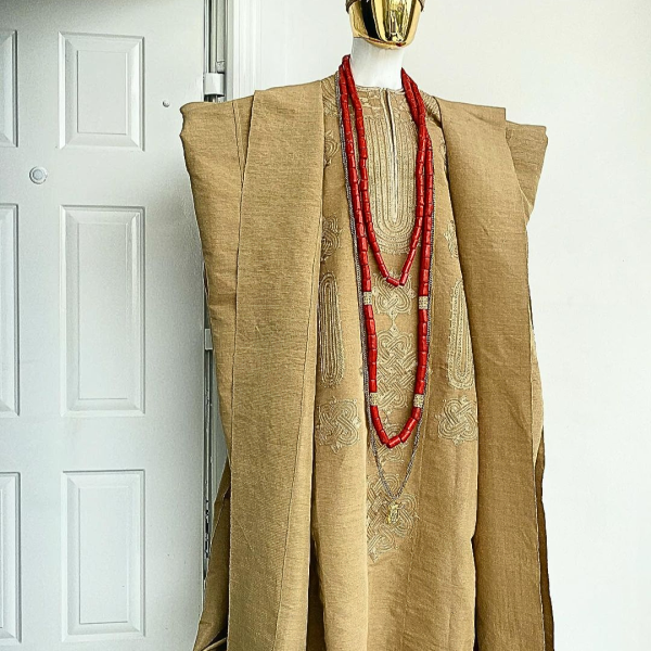 A champagne gold aso oke regal agbada, dashiki, sokoto, red and gold mix coral bead, matching hand woven Yoruba hat, and a long gold chain with a Jesus piece.